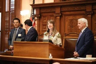 Rep. Anulewicz speaks from the Speaker's Podium alongside Director General Wang and others.