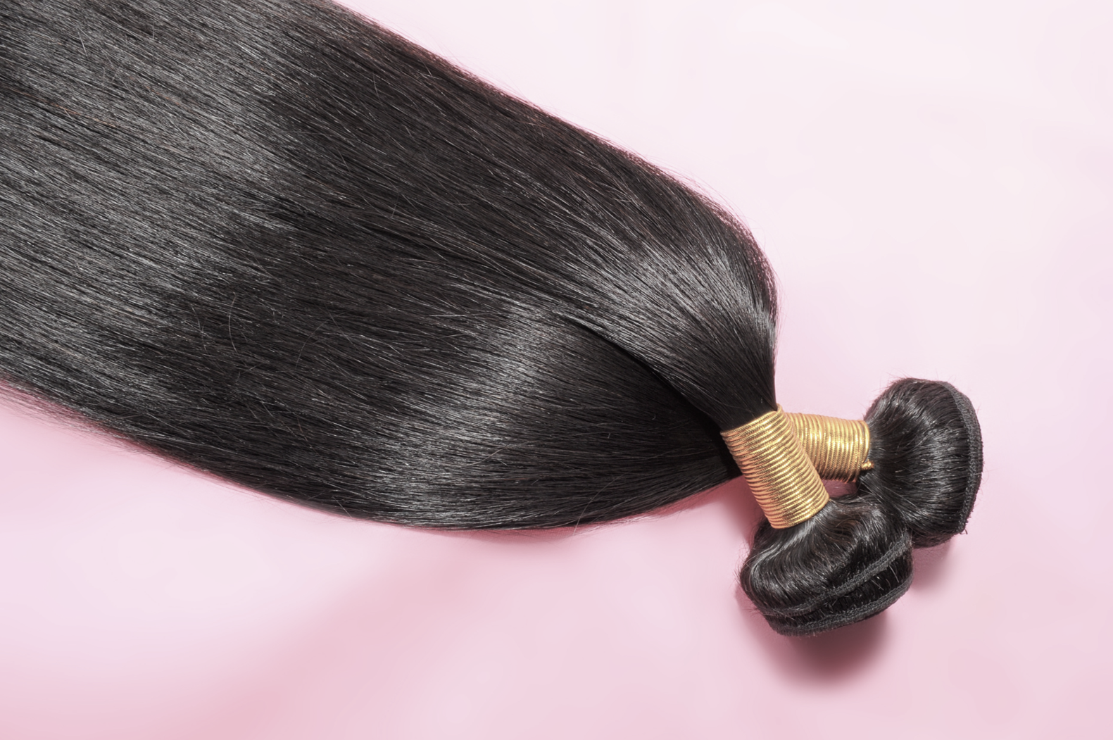 long dark hair extensions laid out on a pink background