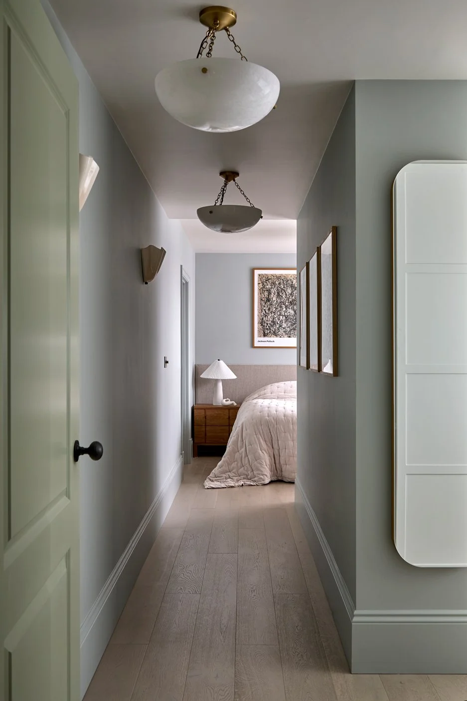 View through the primary bedroom hallway towards the bed, with wall and ceiling lighting.