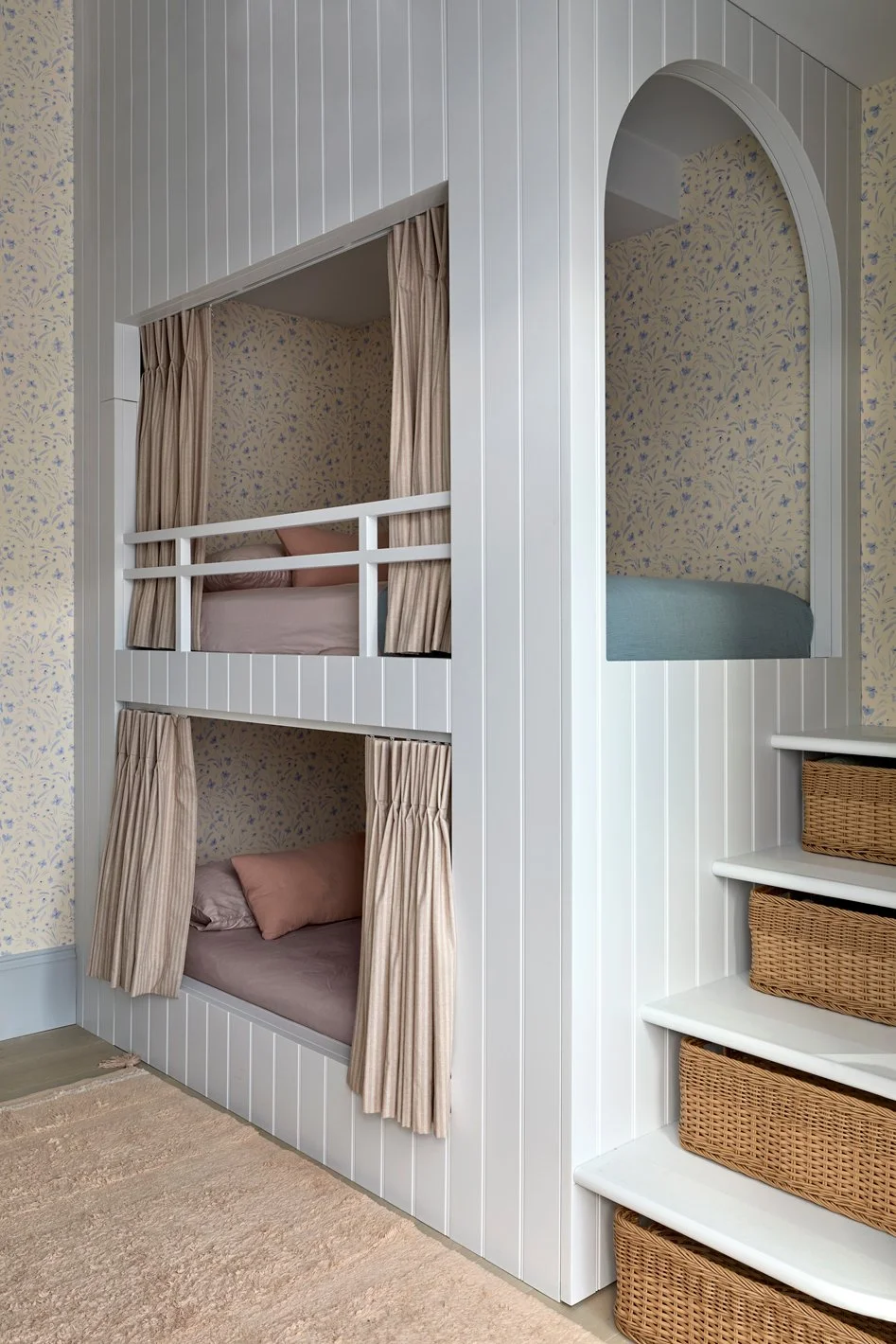 Girls’ bedroom with bespoke bunk beds, privacy curtains and floral wallpaper, viewed from the doorway.