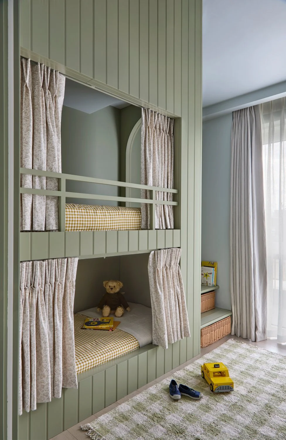 Green bespoke bunk bed joinery with integrated stair storage, woven basket and detailed panelling.