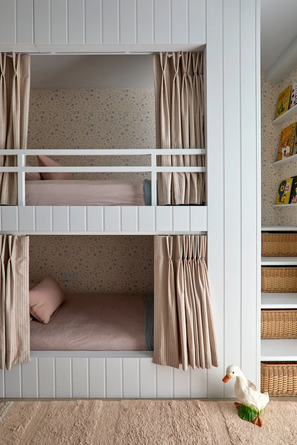 Front view of bespoke panelled bunk beds with curtains and floral wallpaper in a girls’ bedroom.