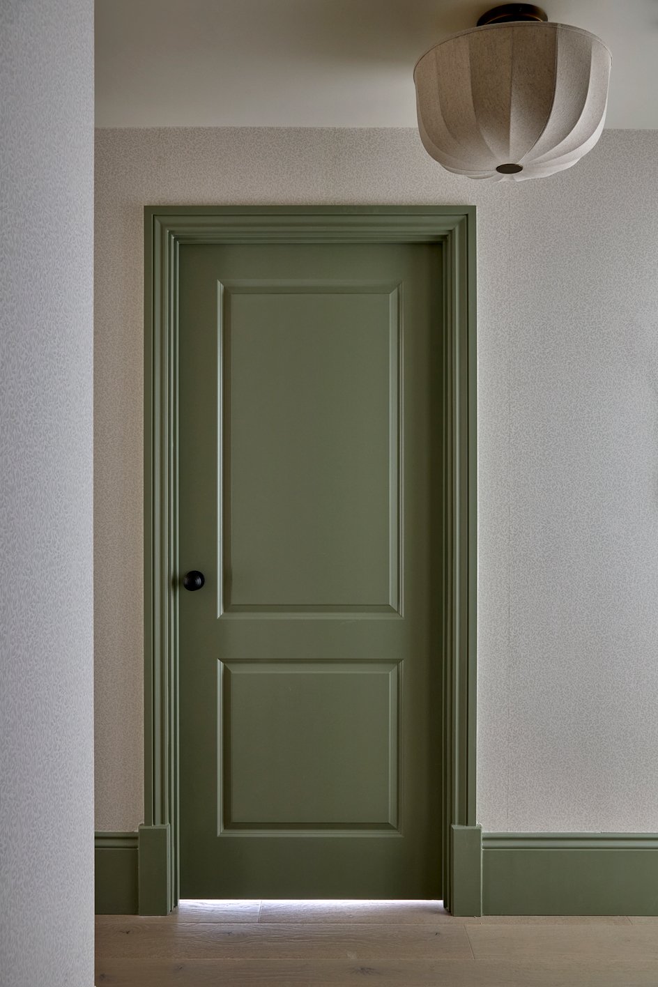 Hallway with contrasting green painted woodwork and subtle patterned wallpaper.