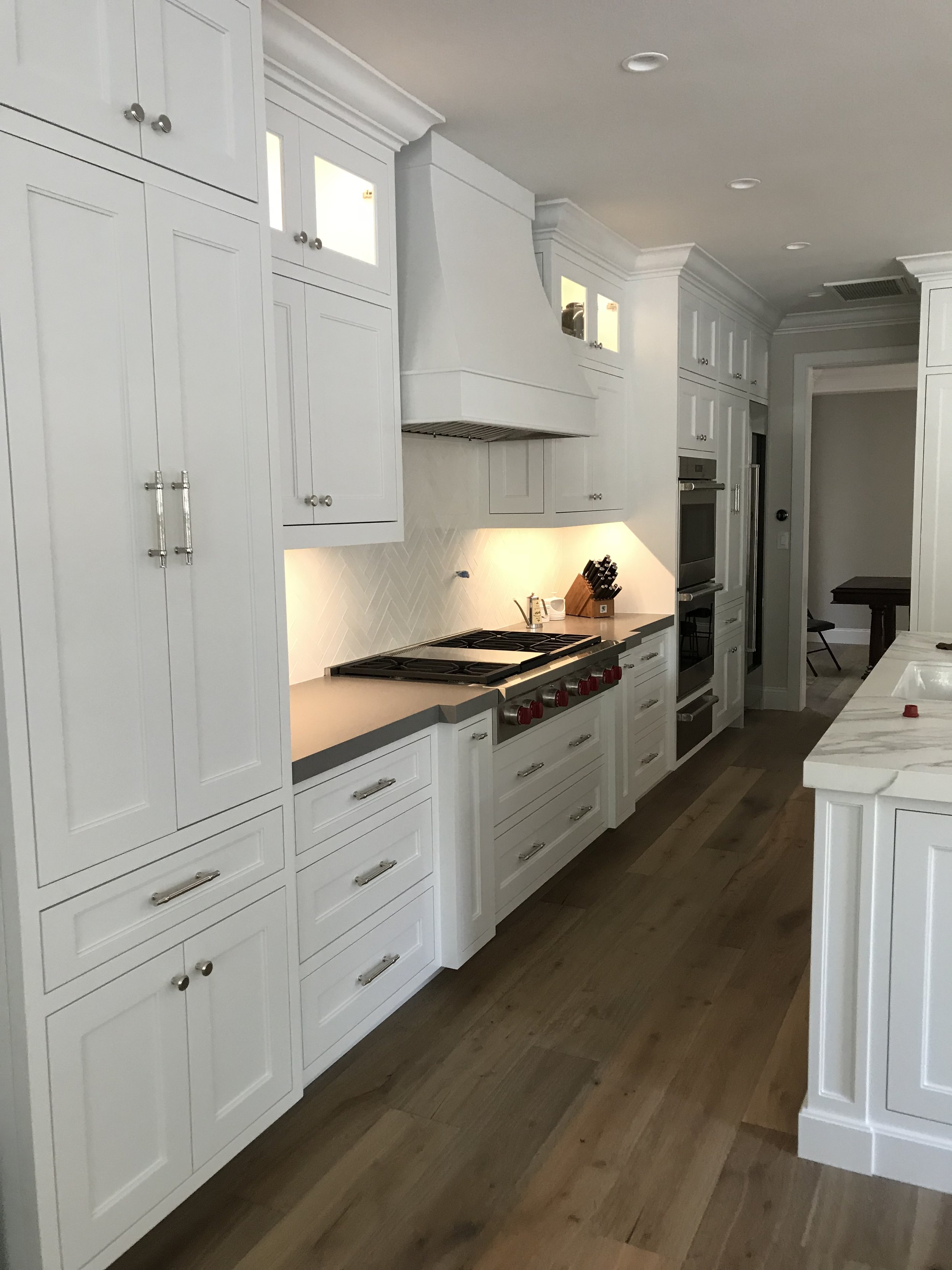Modern kitchen with white cabinets, stainless steel appliances, and wooden flooring.