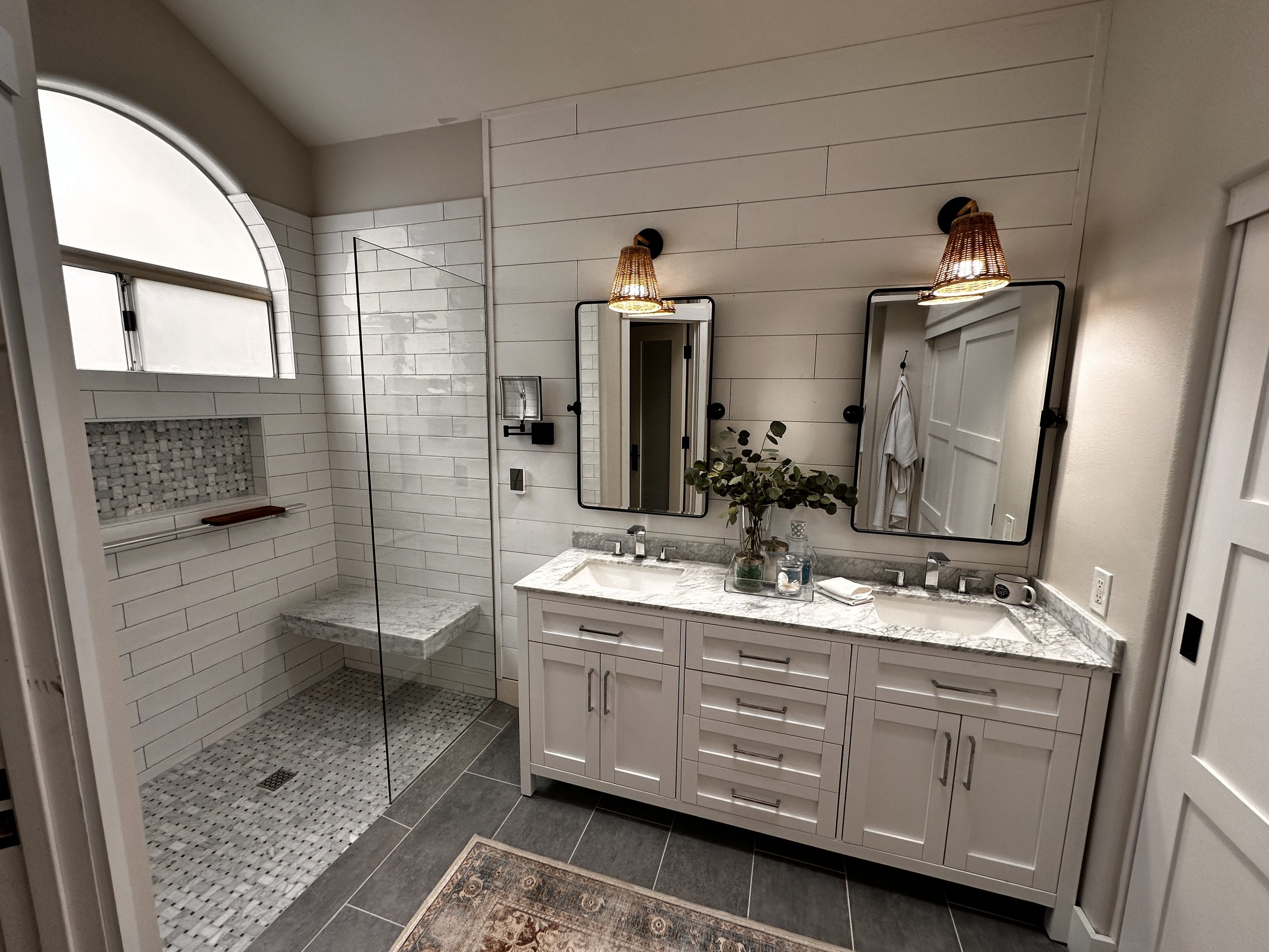 Bathroom with a double vanity, large mirror, wall sconces, and a walk-in shower with white subway tile and a glass door.