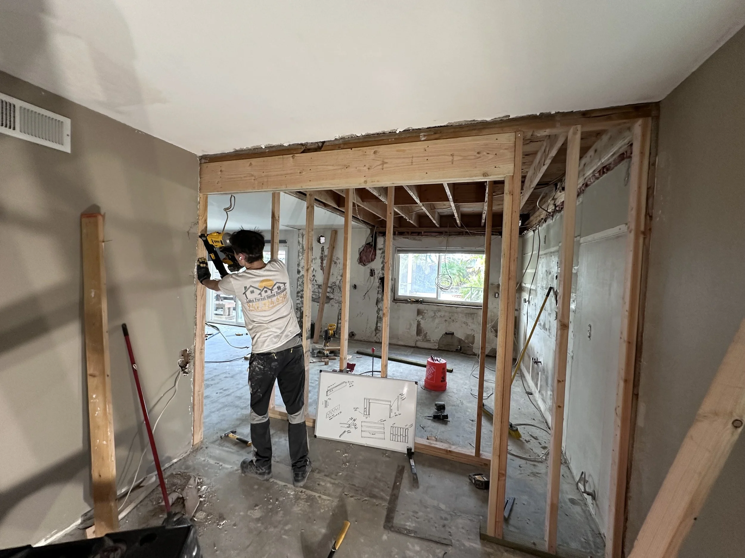 A person working with a drill on a wooden frame structure inside a house renovation project.