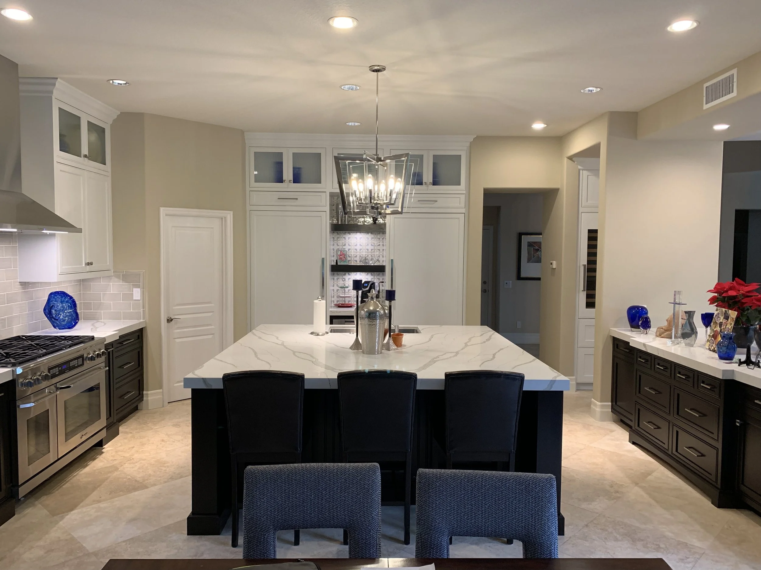 A modern kitchen with white cabinets, a marble island, black dining chairs, and decorative blue glassware on the counters.