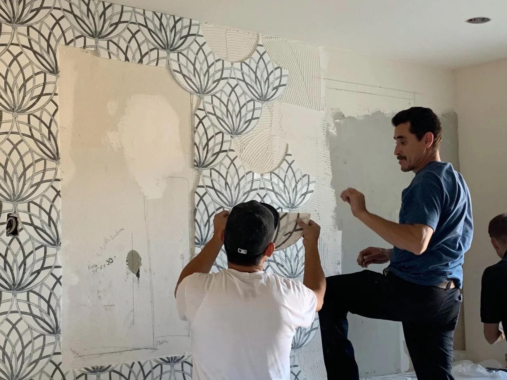 People installing water jetted marble mosaic decorative tiles with a geometric design in a primary bathroom under construction.
