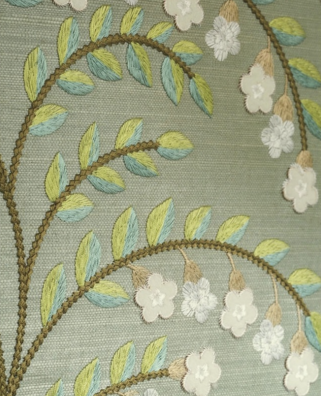 Close-up of embroidered fabric featuring a pattern of green and blue leaves and white flowers on a light green background.