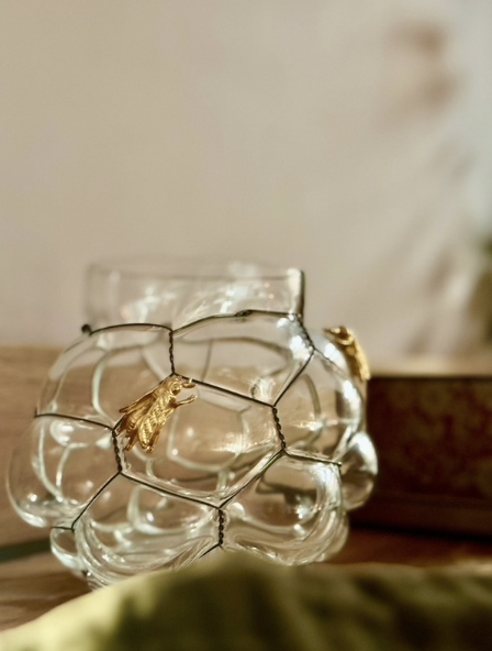 A glass container shaped like a honeycomb with a string of fairy lights and decorative bees attached