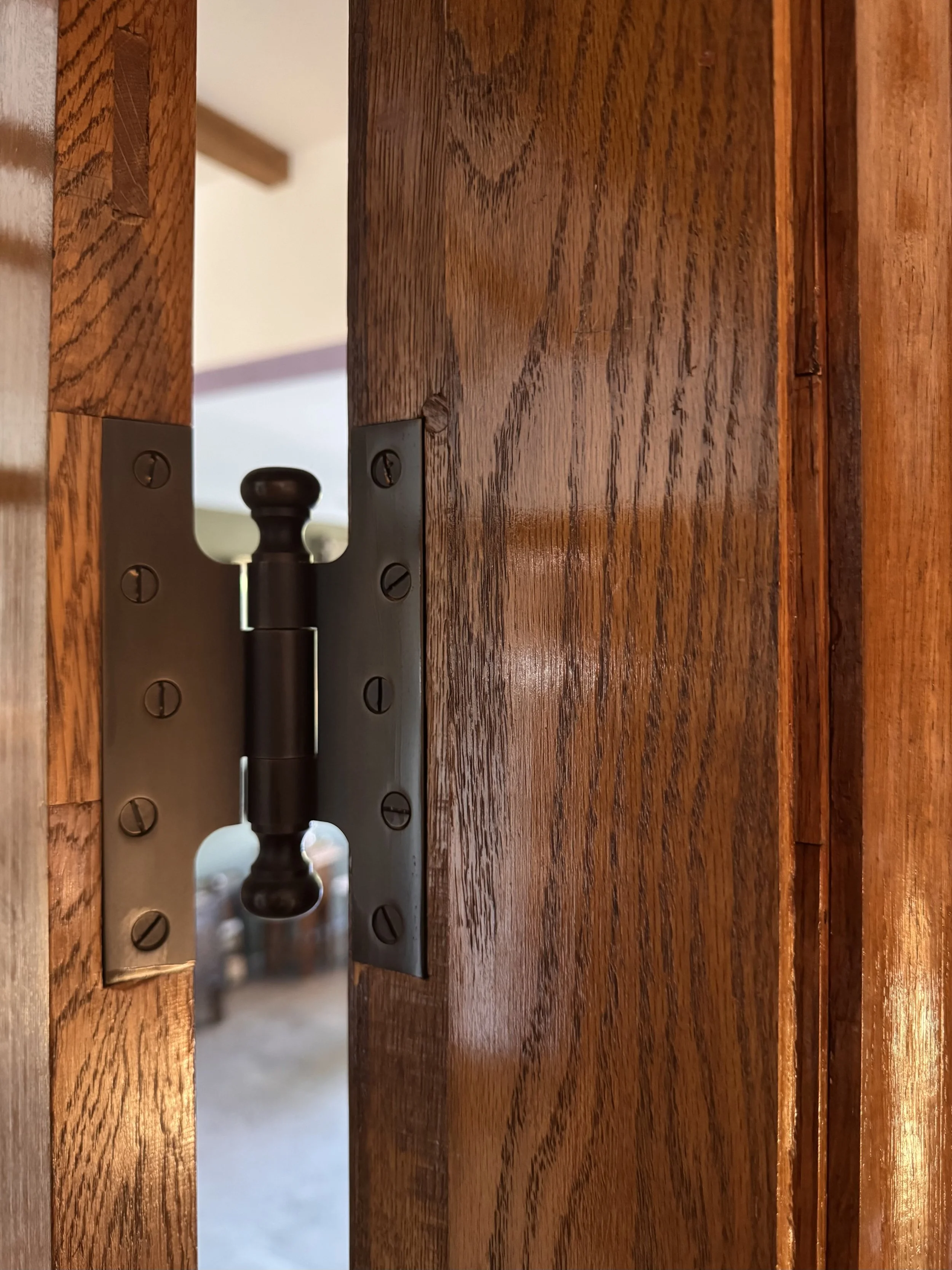 Close-up of a wooden door with a metal hinge and a dark knob visible through a crack in the door.