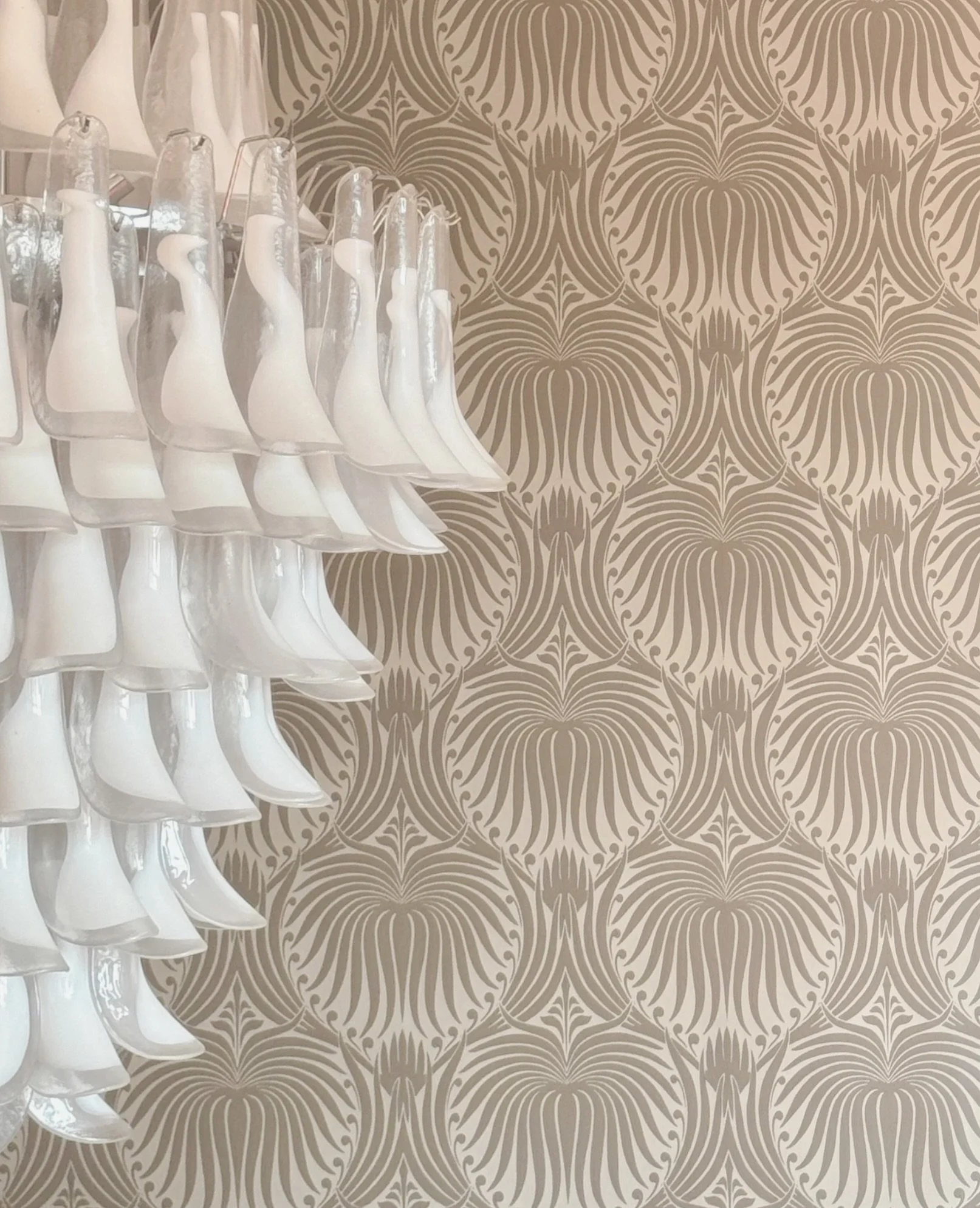 A set of clear glass glasses with white swan-shaped bases and white liquid inside, lined up against a patterned beige wallpaper background.