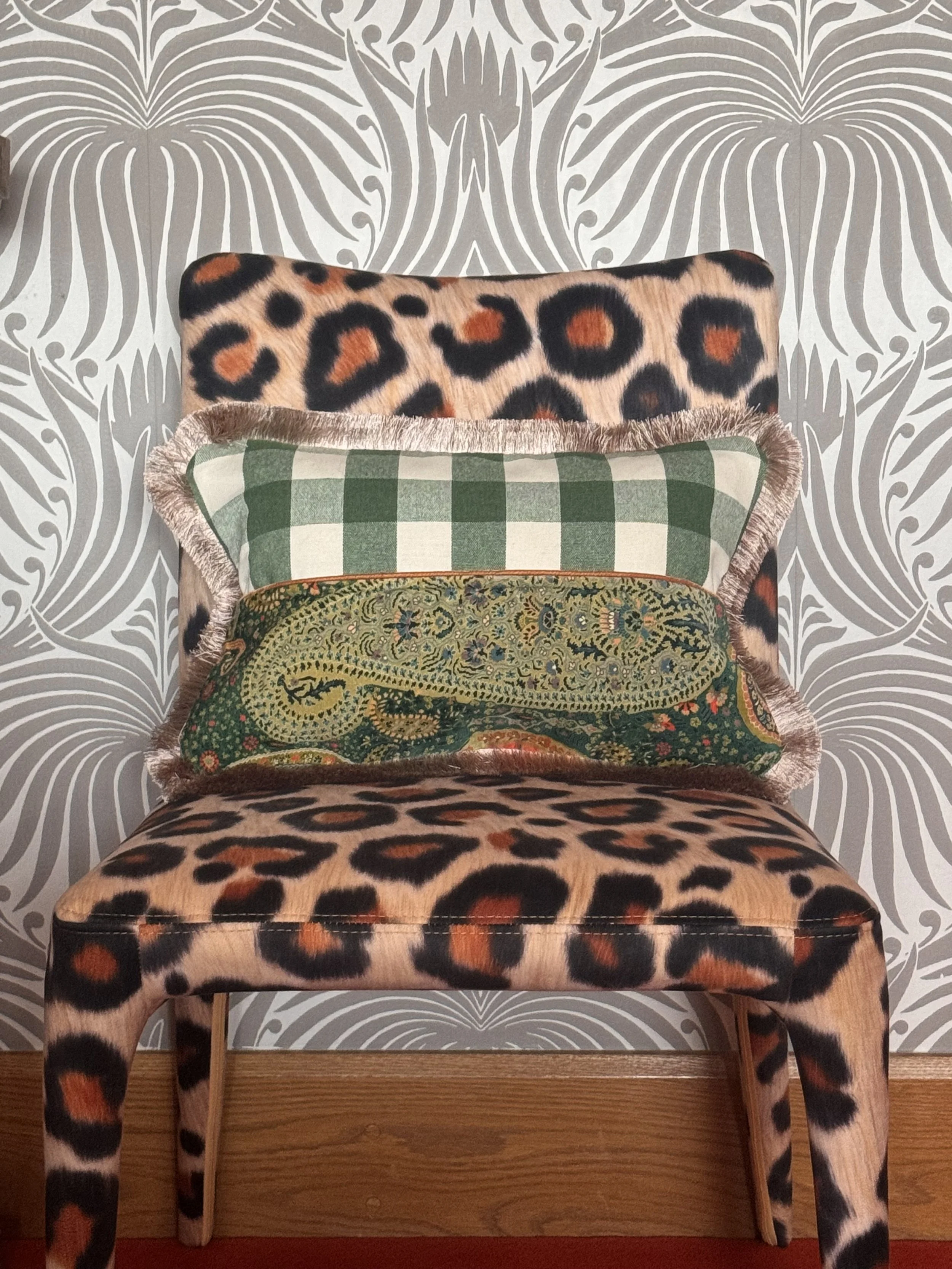 A chair with animal print upholstery featuring leopard and giraffe patterns, placed against wallpaper with a symmetrical floral design in gray and white.