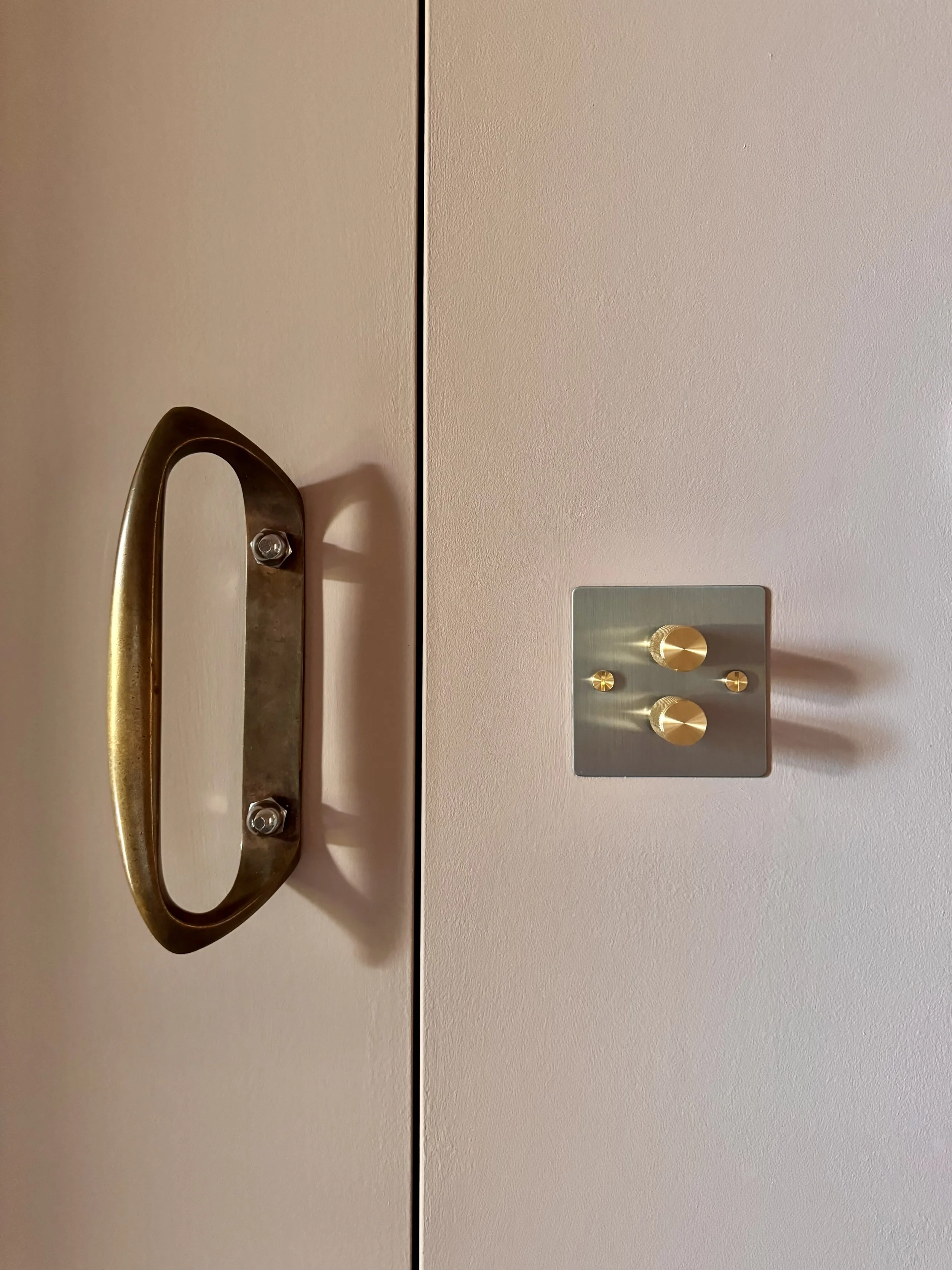 Close-up of a door with a brass handle on the left and a silver switch panel with three gold knobs on the right.