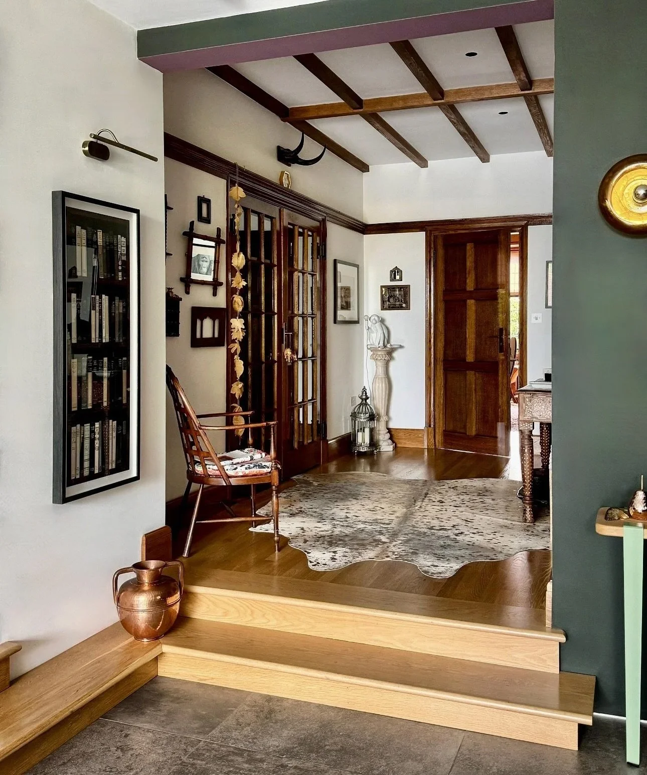 Interior view of a an Arts & Craft period property home entryway with wooden steps, a cowhide rug, decorative items, art and a mix of vintage and modern decor.