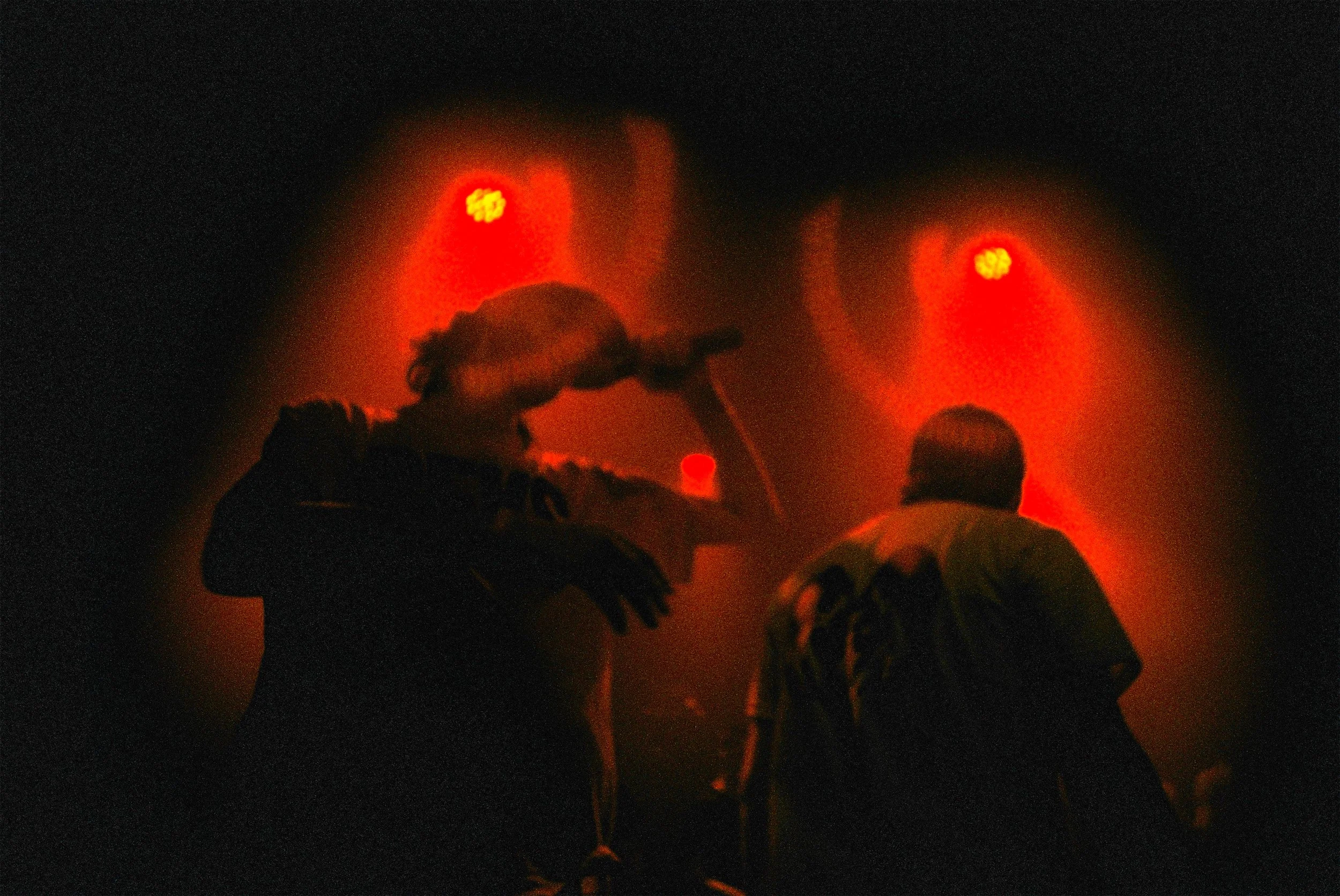 Silhouettes de personnes regardant un spectacle pyrotechnique avec des explosions lumineuses rouges dans le ciel nocturne.