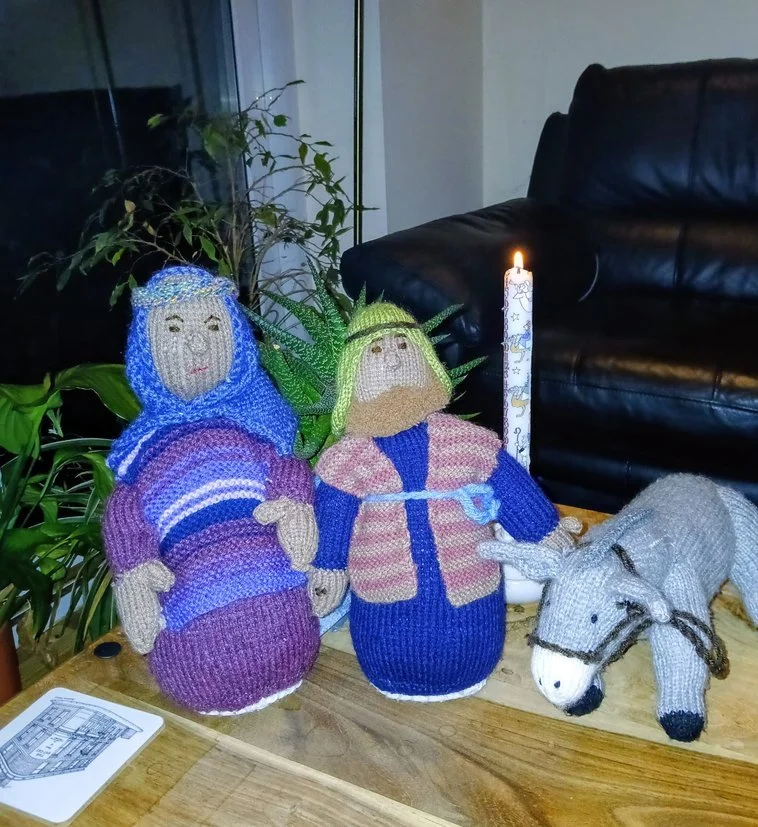 Knitted nativity scene figures including Mary, Joseph, and a donkey on a wooden table.