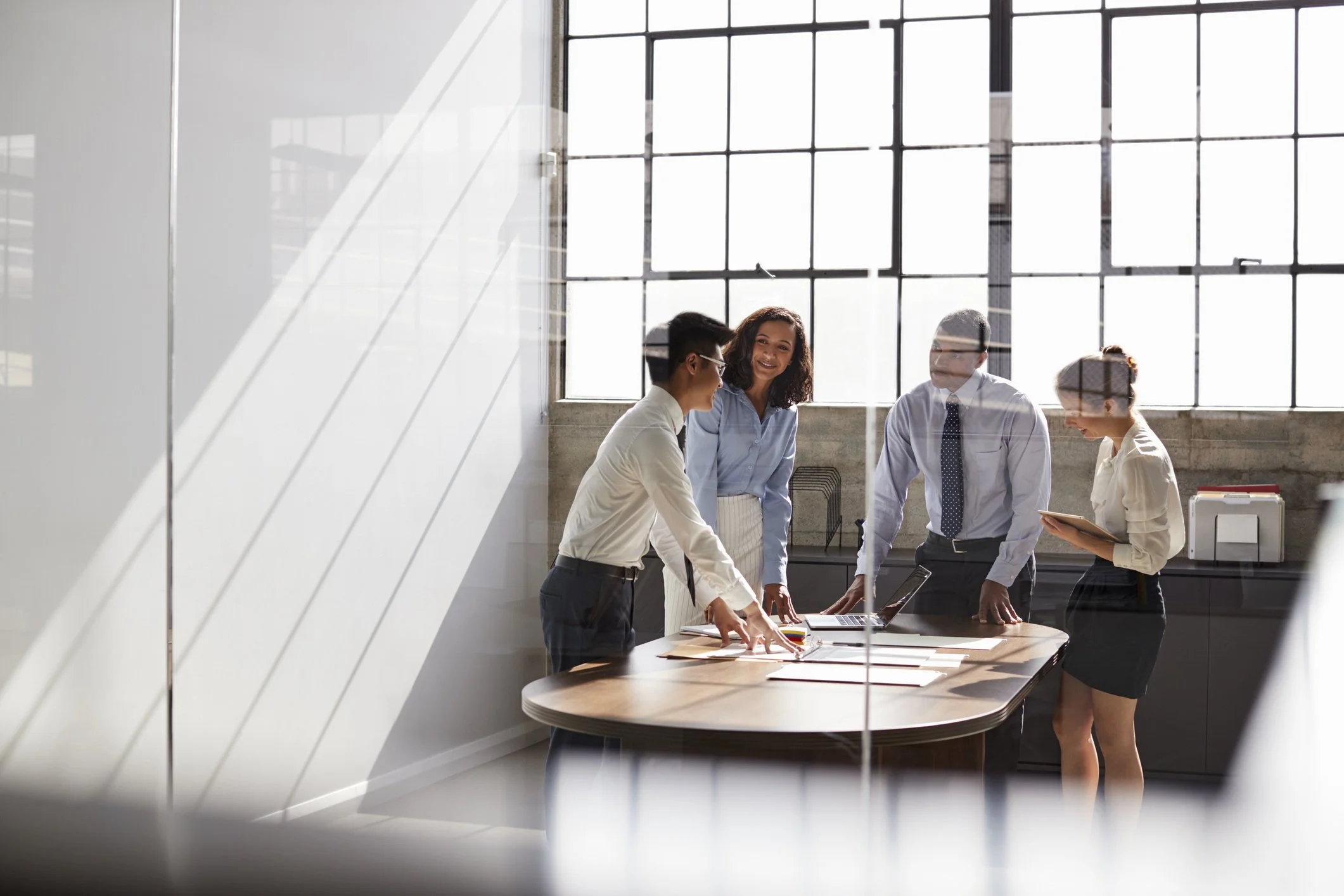 Business team meeting in a bright office, viewed through a glass wall with reflected window panes.