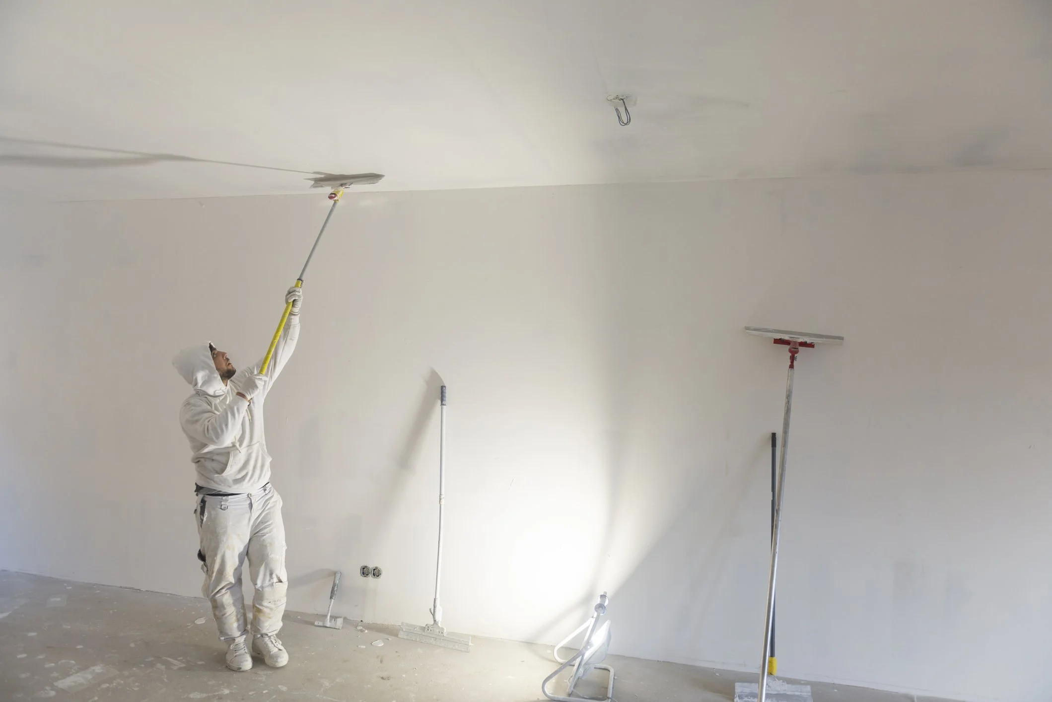 A skilled artisan meticulously paints a ceiling with a large roller, exemplifying NGage Properties Group's commitment to painting and wall covering services of unparalleled craftsmanship and sophistication.
