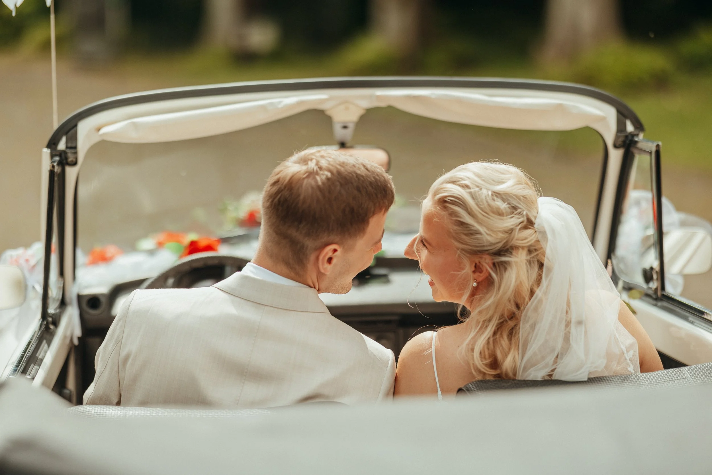 Ein Brautpaar fährt in einem offenen weißen Cabrio bei einer Hochzeit.
