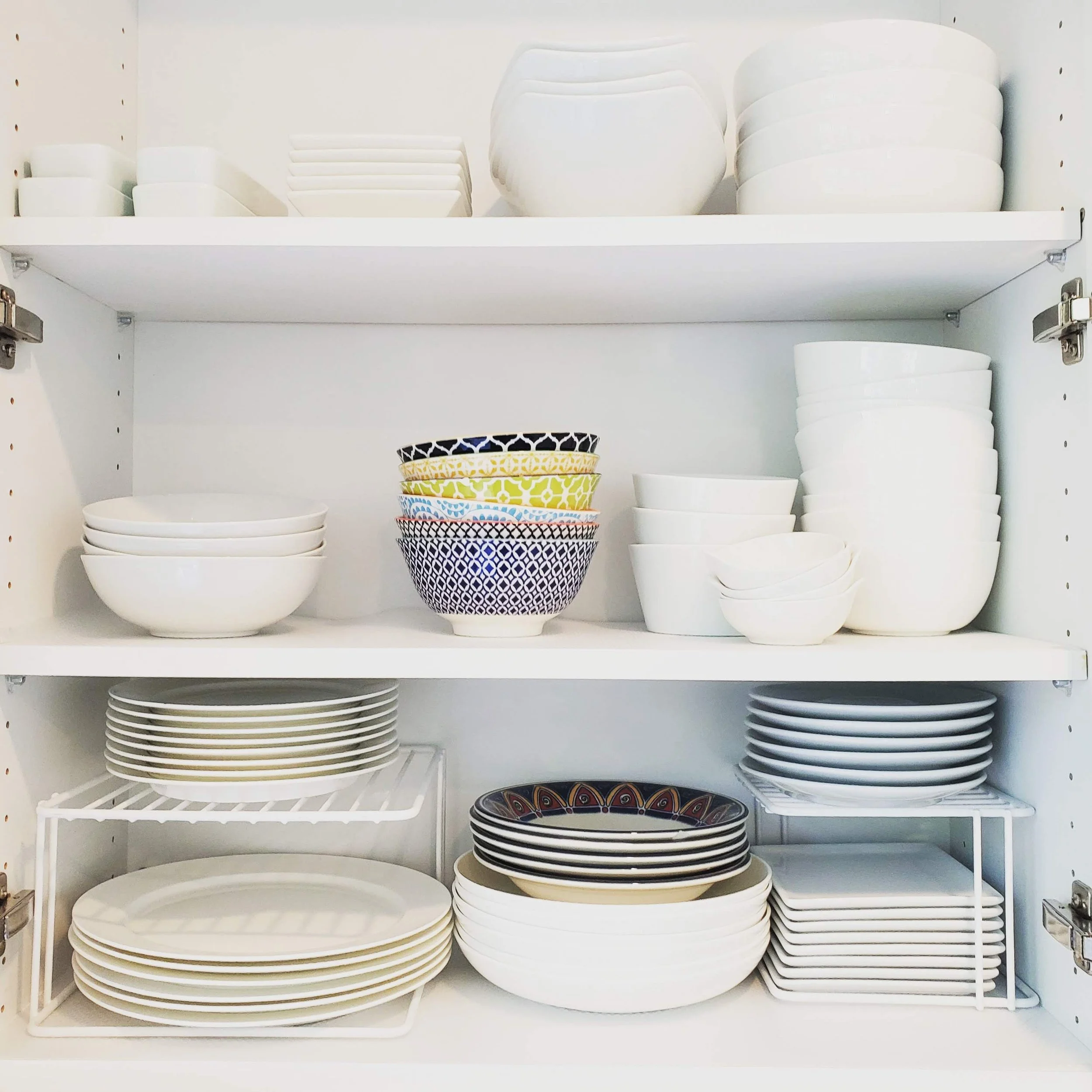 Shelves with white bowls and plates, some decorated, stored vertically and stacked neatly.