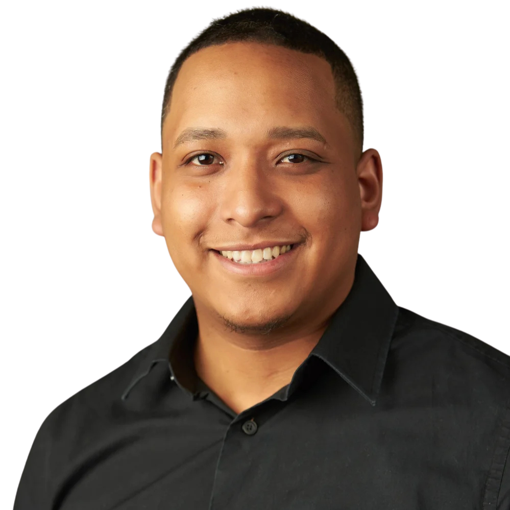 Portrait of a smiling young man with short dark hair, wearing a black button-up shirt, against a light gray background.