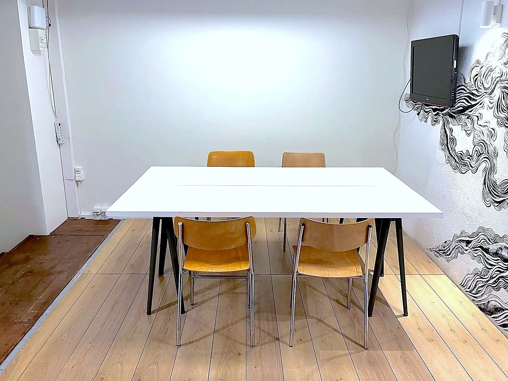 Salle Betty à Genève en configuration réunion pour 2 personnes, table blanche, écran et fresque murale