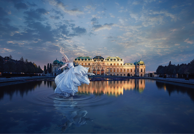 A woman in a white flowing dress dancing in a fountain in front of an ornate historical building during twilight.