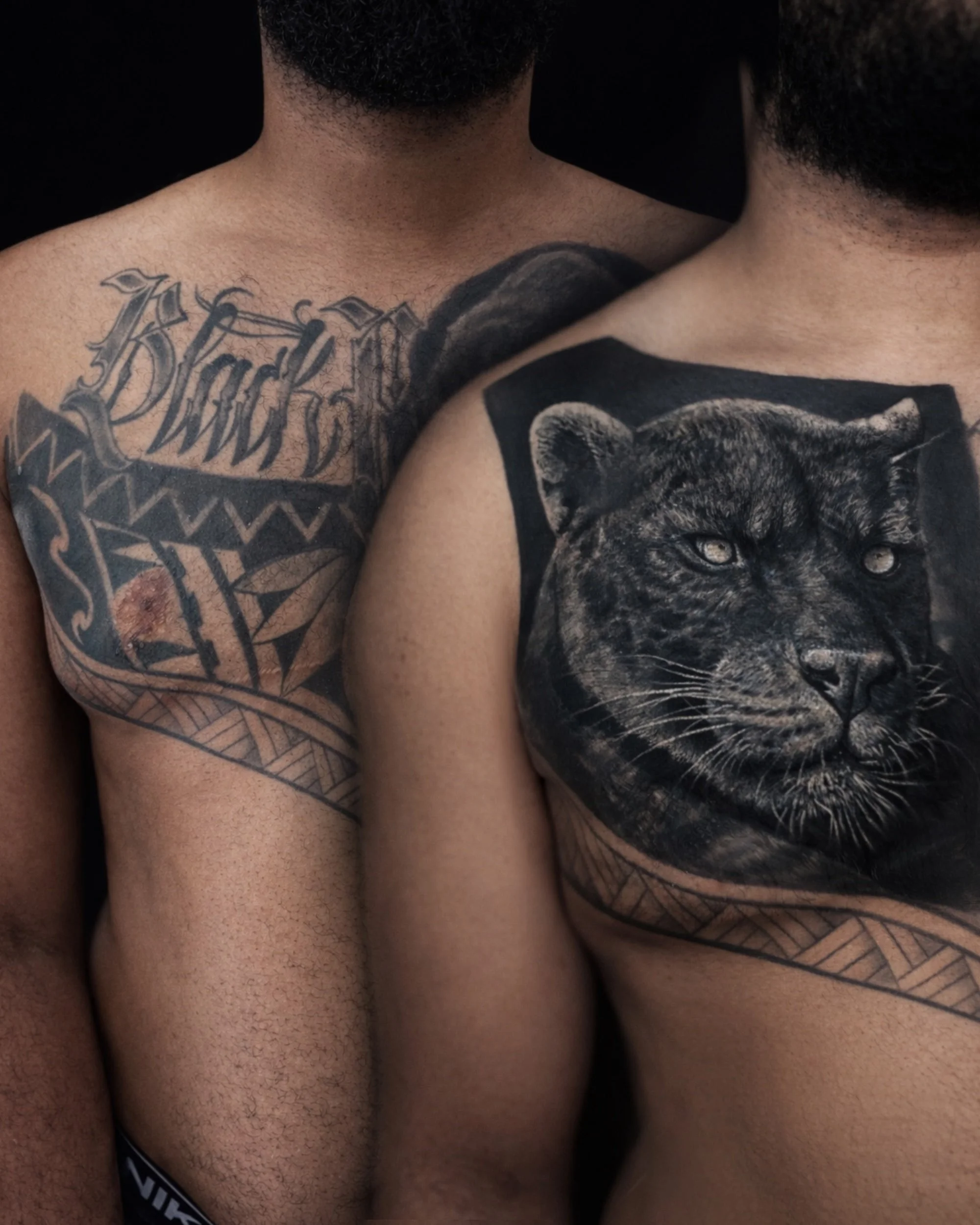 Zwei Männer mit Tattoos auf der Brust und Schulter, einer mit einem Panther-Tattoo und der andere mit einem Tattoo mit Schriftzug und geometrischen Mustern.