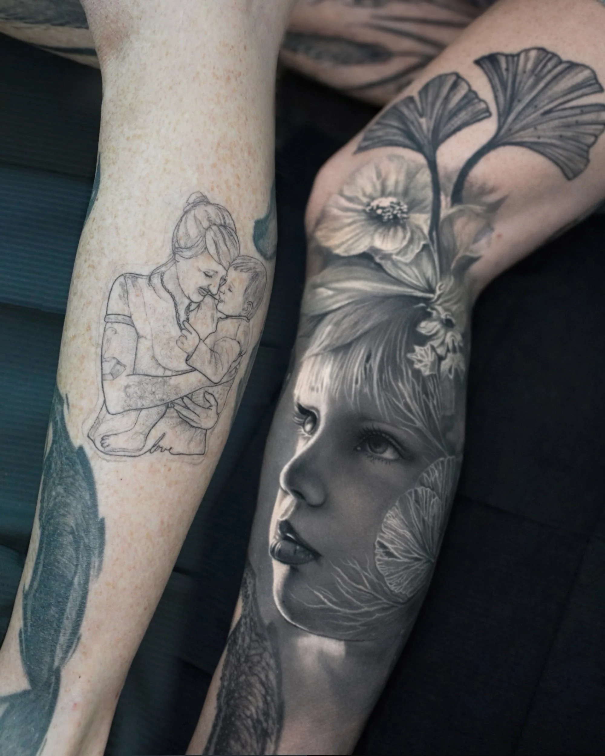 Zwei tätowierte Unterarme, links eine einfache Linienzeichnung einer Frau, die ein Kind hält, rechts eine realistische Schwarz-Weiß-Tätowierung eines Kindergesichts mit Blumenmuster.