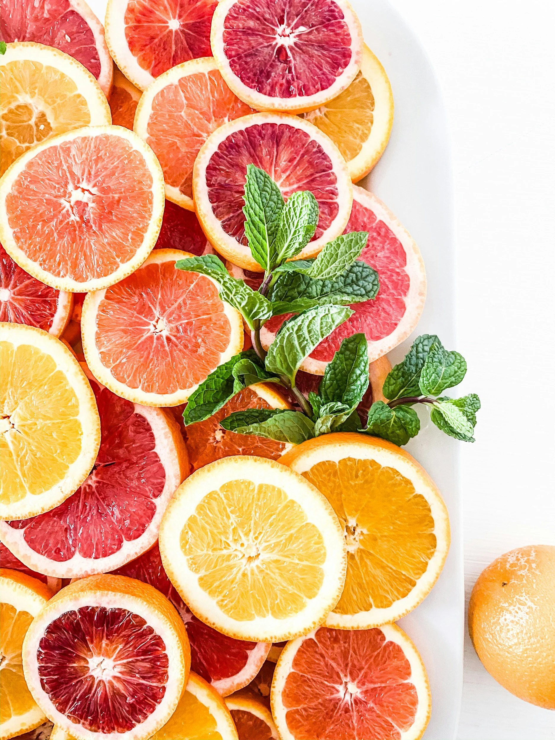 A plate of sliced citrus fruits including blood oranges, grapefruits, and oranges, garnished with fresh mint leaves.
