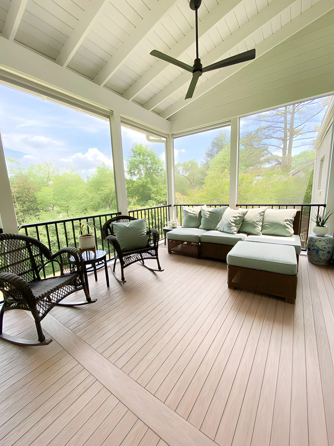 Screened-in porch with wicker chairs, an outdoor sofa, ceiling fan, and view of trees and blue sky