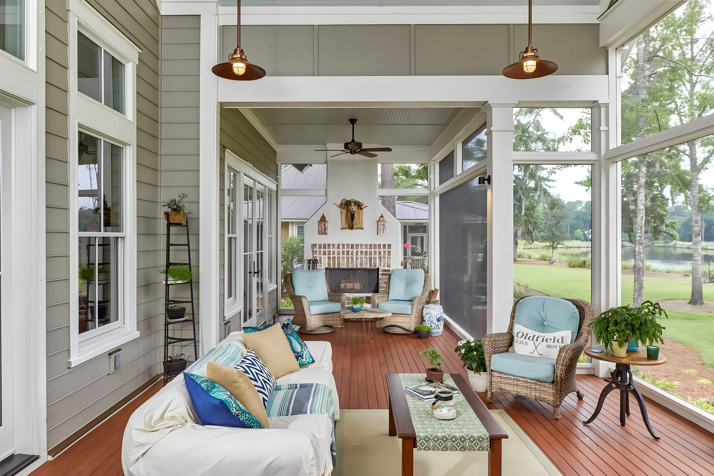 Screened-in porch with wicker and upholstered furniture, a fireplace, and a view of a grassy yard with trees and a lake.
