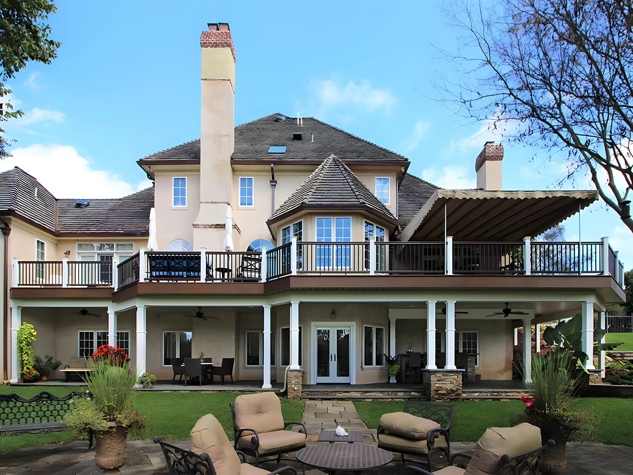 Backyard of a large, multi-story house with a patio, outdoor furniture, and landscaped garden.