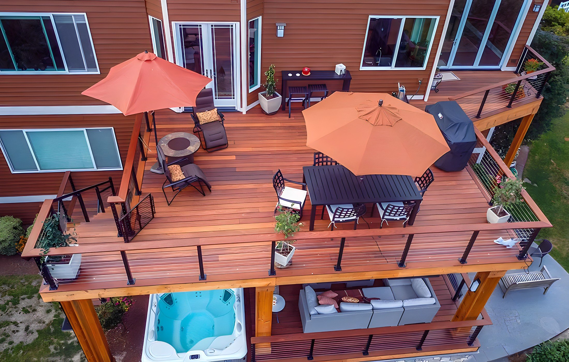 A multi-level outdoor deck attached to a house, featuring a hot tub, outdoor furniture, umbrellas, potted plants, and various seating arrangements.