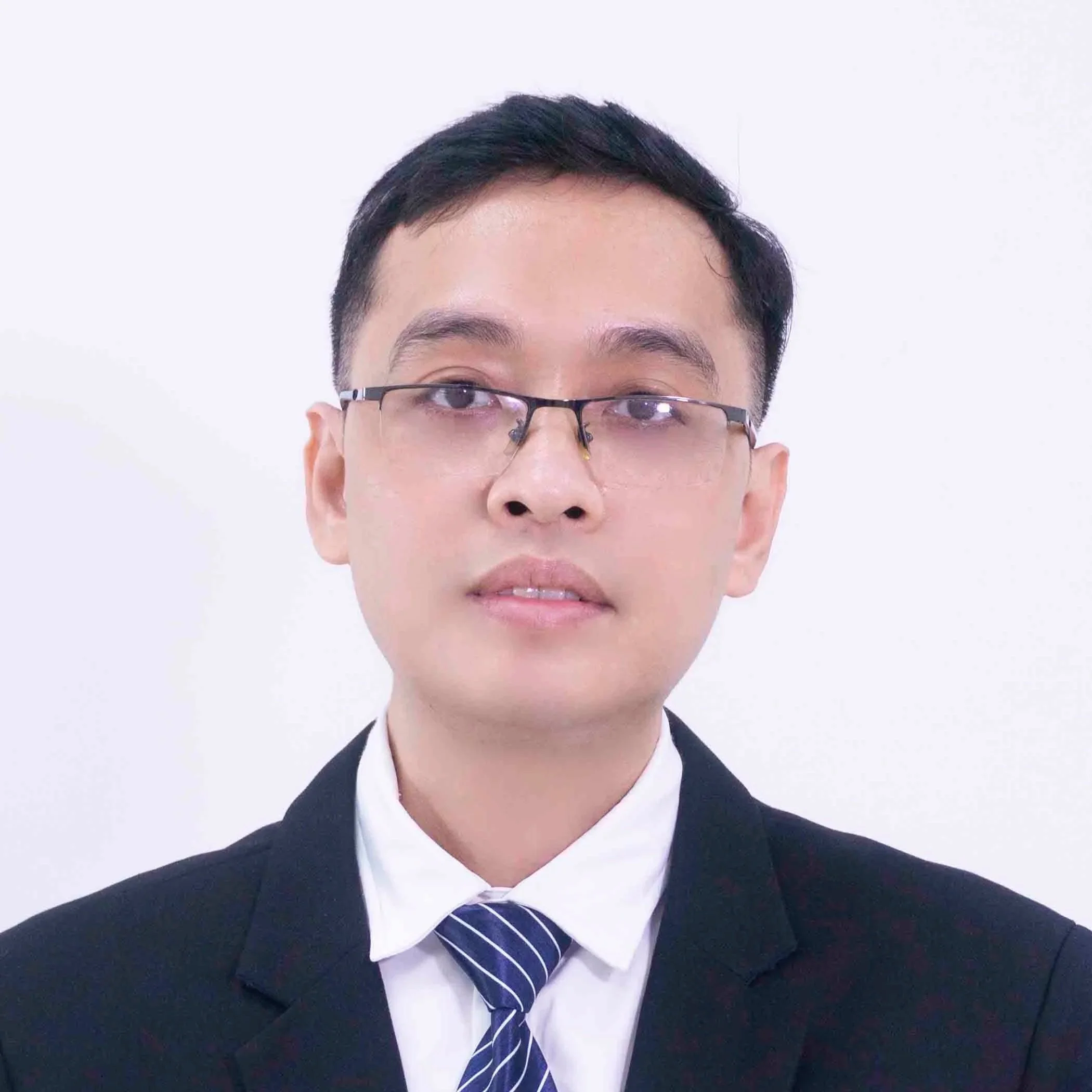 Young man wearing black suit, white shirt, blue striped tie, and black glasses, looking at the camera against a white background.