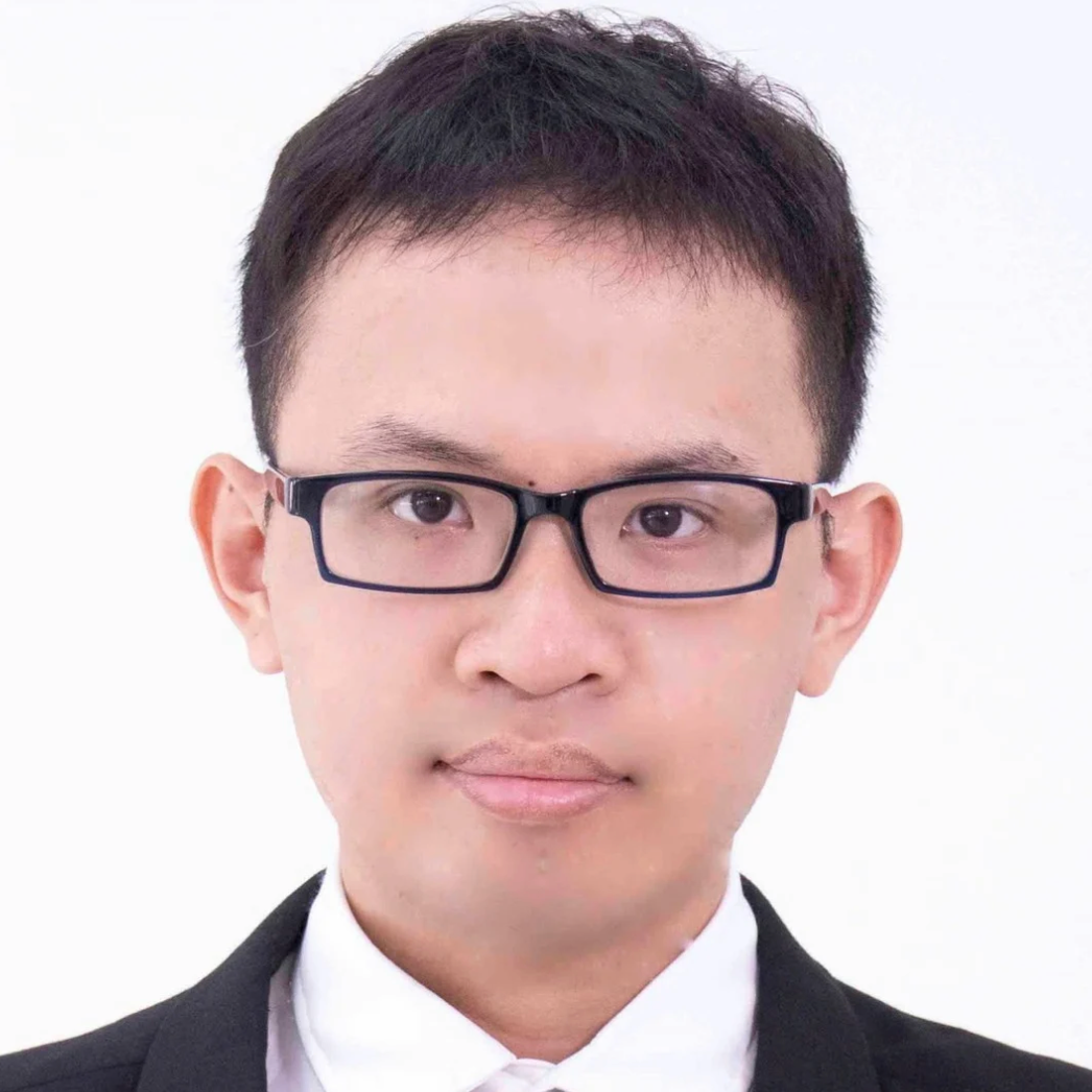 A young man wearing glasses, a black suit, a white shirt, and a navy blue striped tie, posing in front of a plain white background.