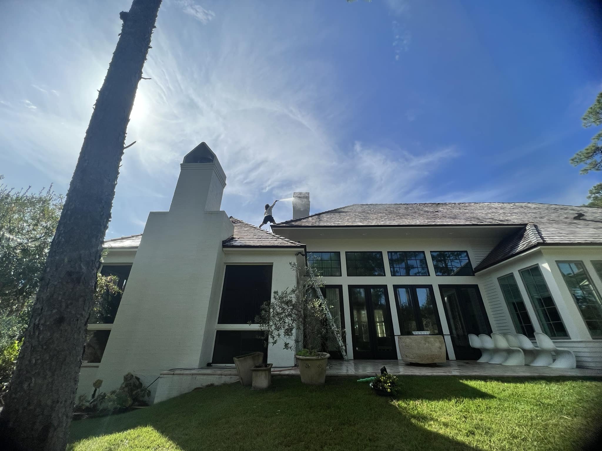 Soft washing a roof on a large home on a beautiful summer day.