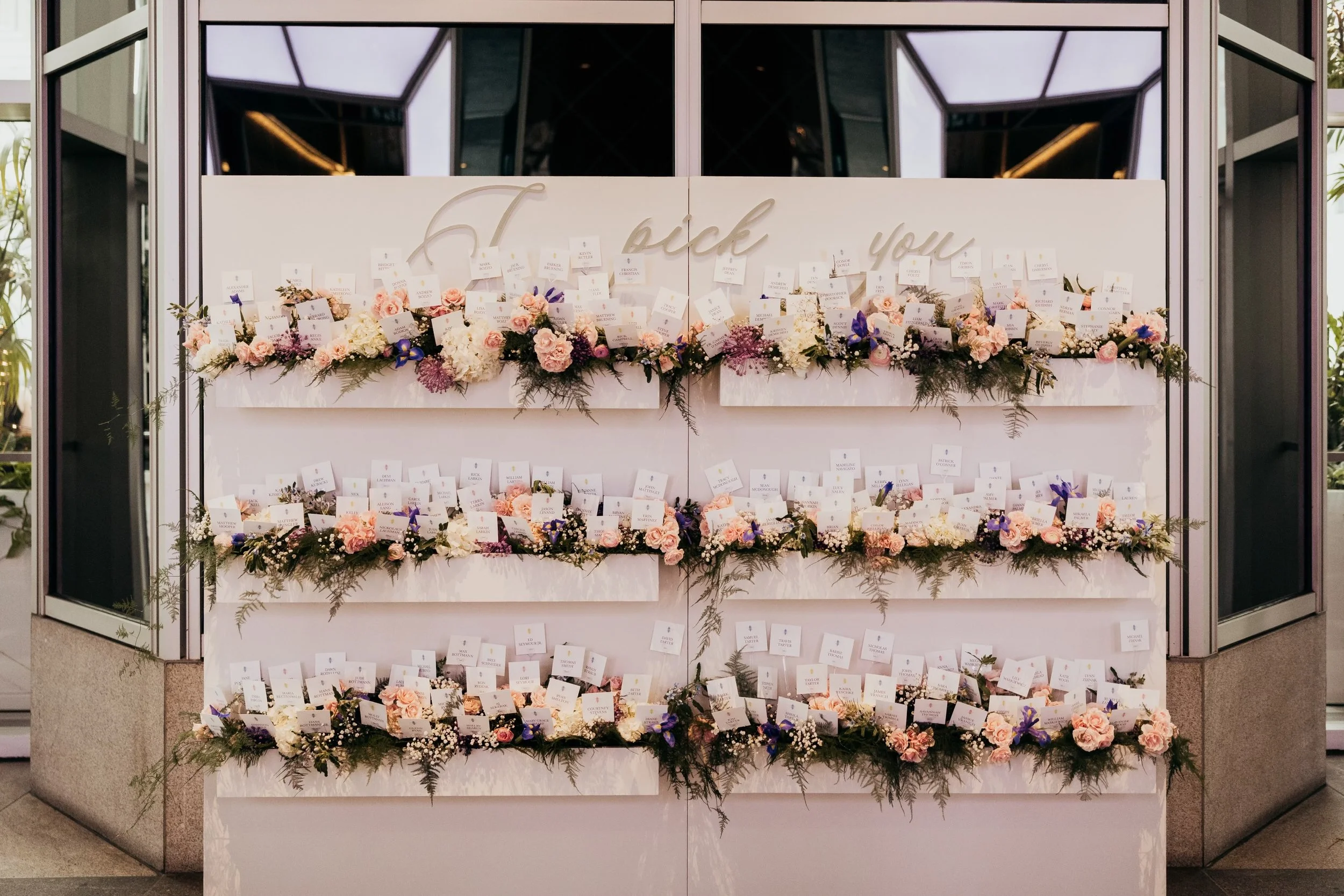 Wedding escort card display with floral arrangements and "I pick you" sign