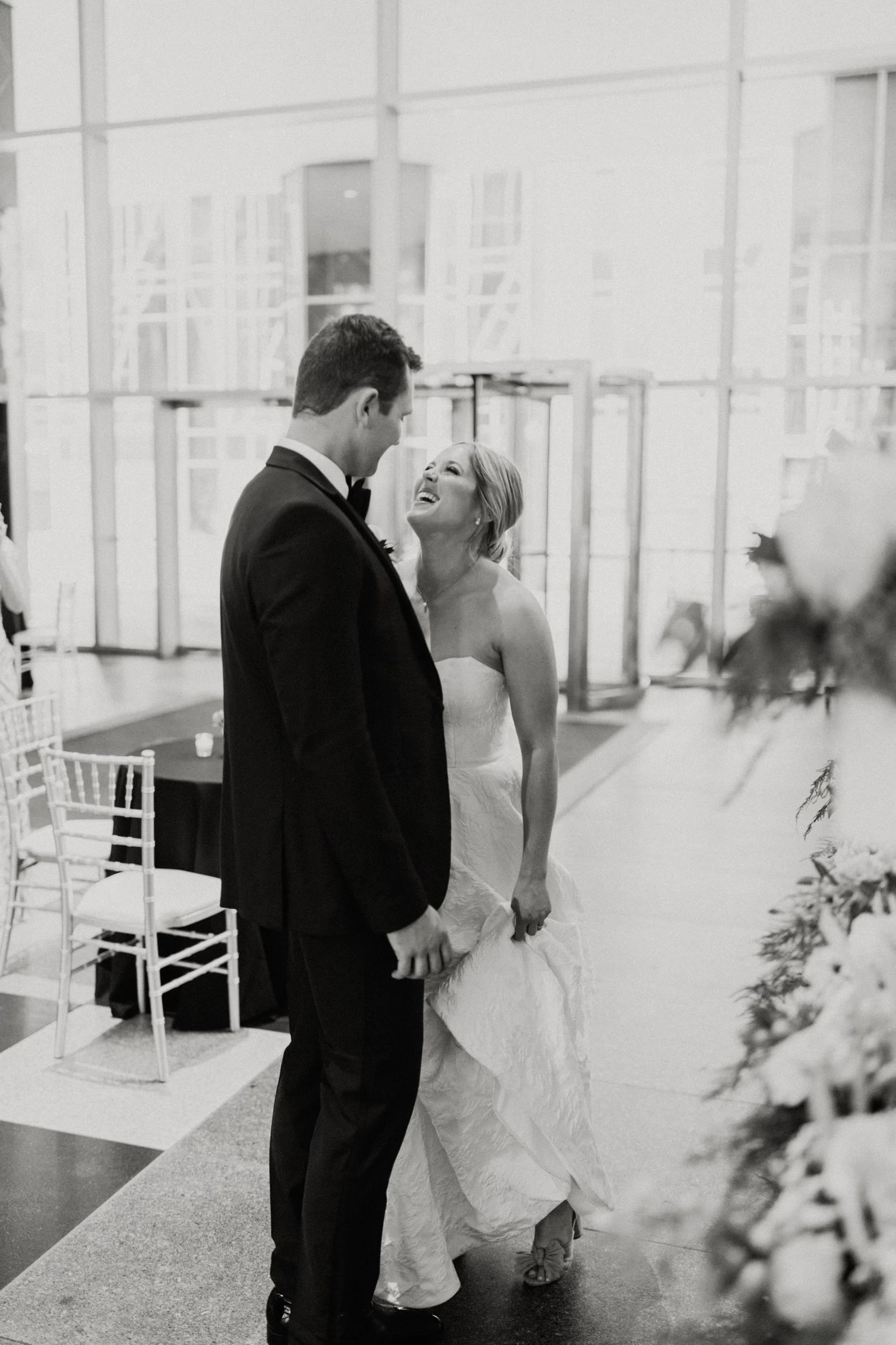 Bride and groom laughing in a modern wedding venue, black and white photo.