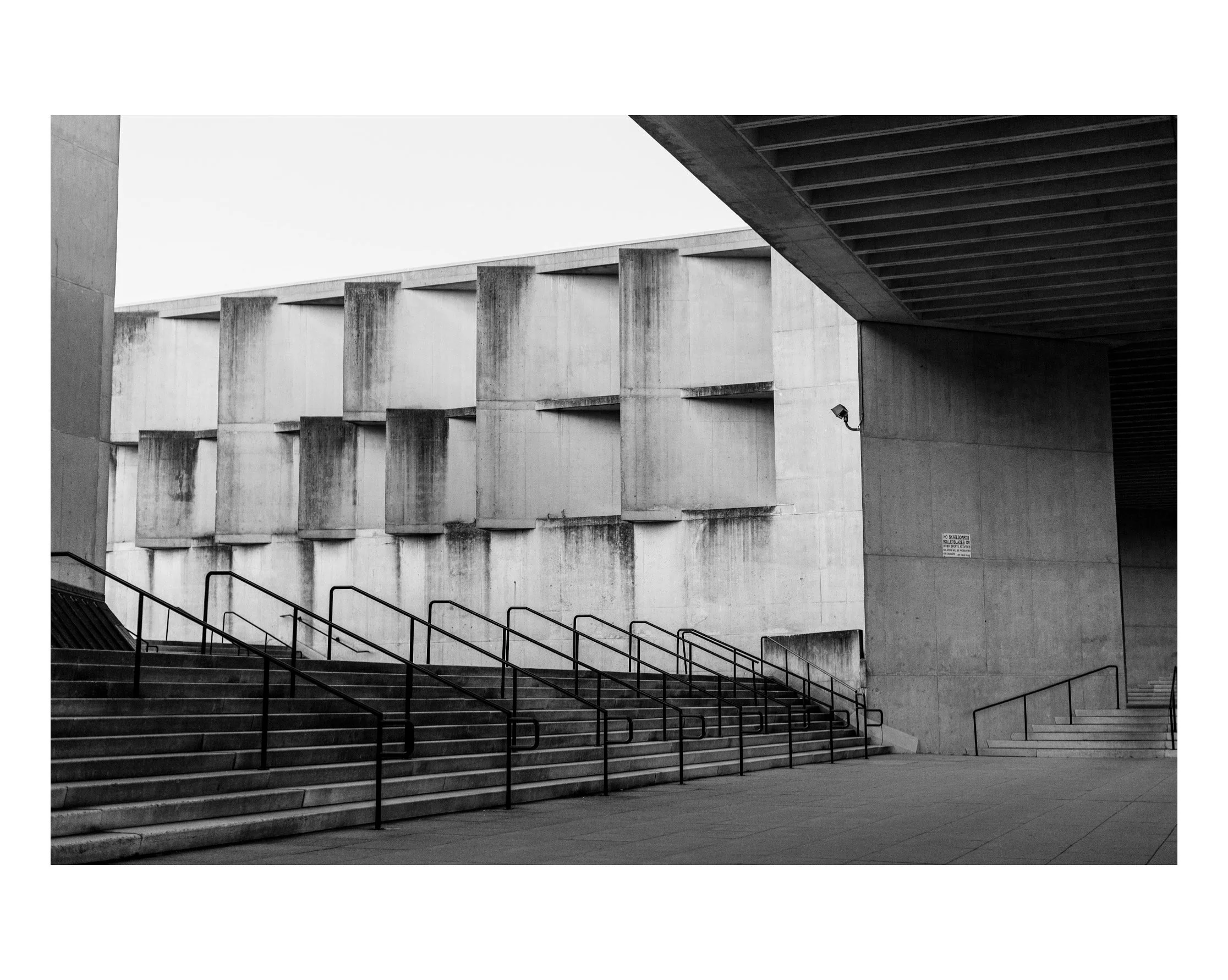 Concrete staircase leading up to a modern building with vertical concrete blocks and a security camera on the wall.
