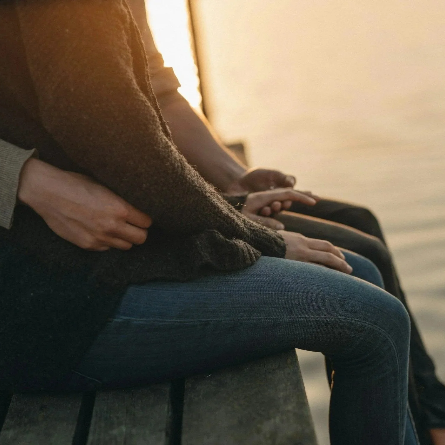 People sitting on a bench by the water, with their hands resting on their laps or clasped together.