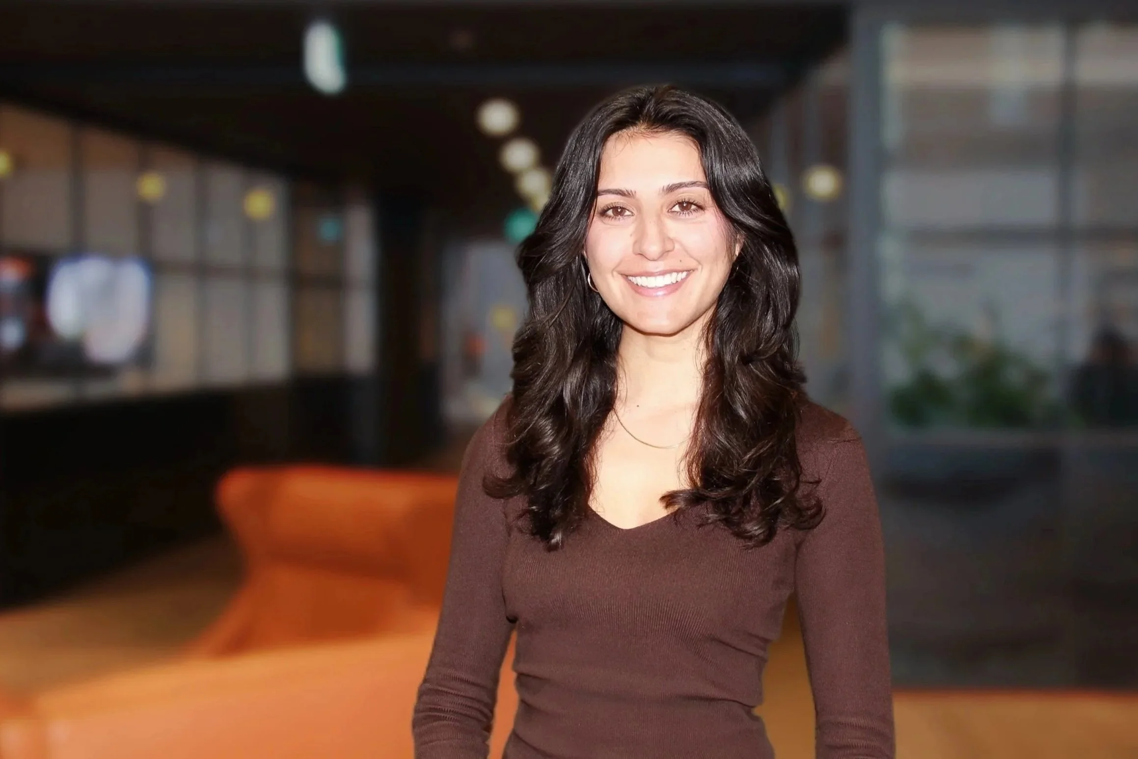 Senior Associate, Asha Keaney smiles at the camera. She has long, dark hair and wears a chocolate brown fitted top.