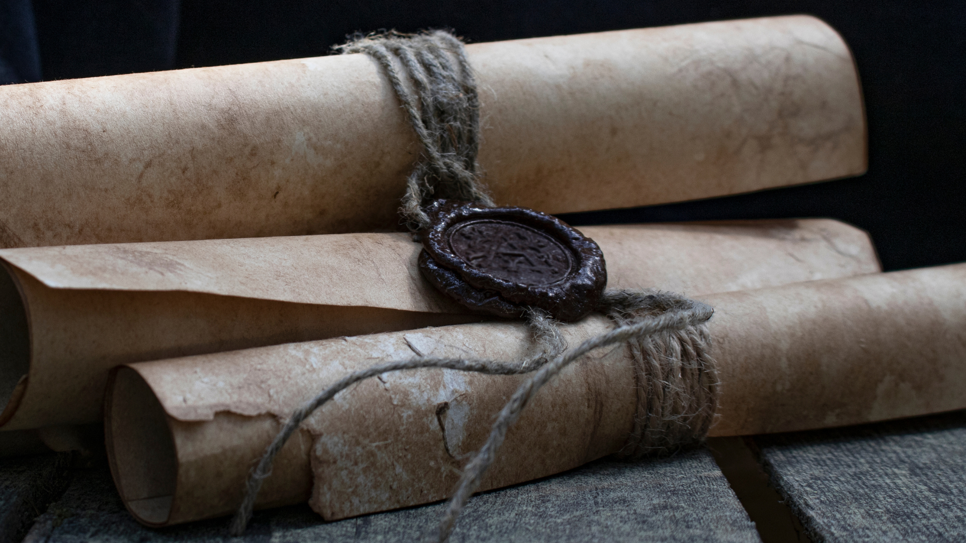 Three rolled parchment scrolls bound with twine, sealed with a dark wax seal embossed with a symbol or insignia.