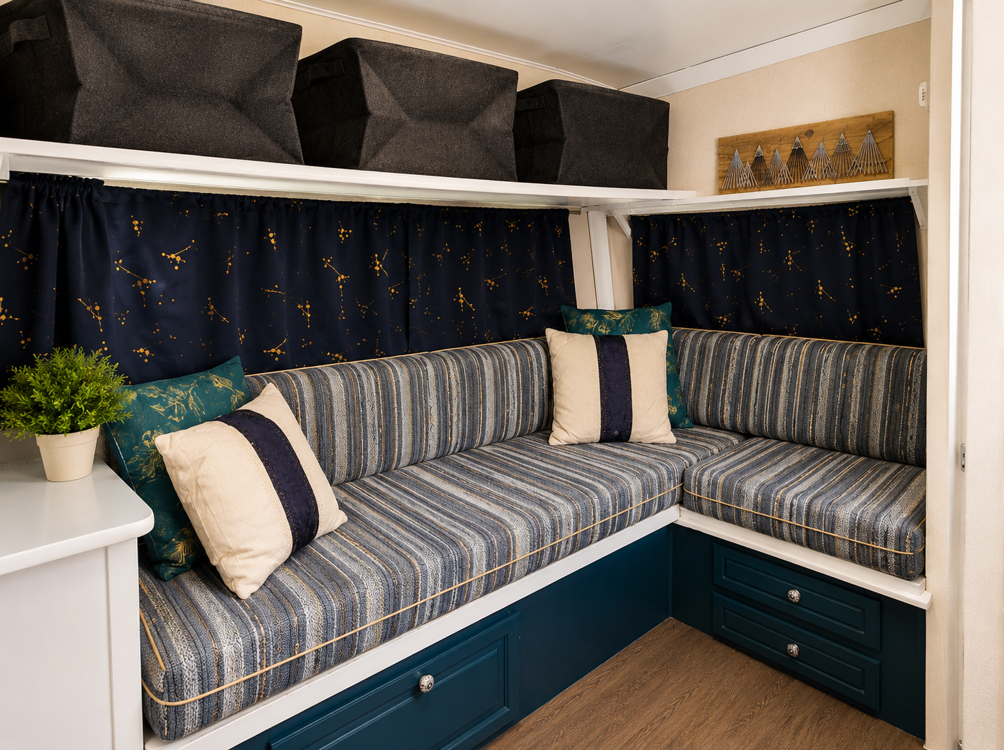A cozy corner with a built-in L-shaped striped fabric couch, above which are black storage boxes and a wooden wall decor. The couch has patterned cushions and is set against a dark blue curtain with yellow star and constellation designs. There is a s
