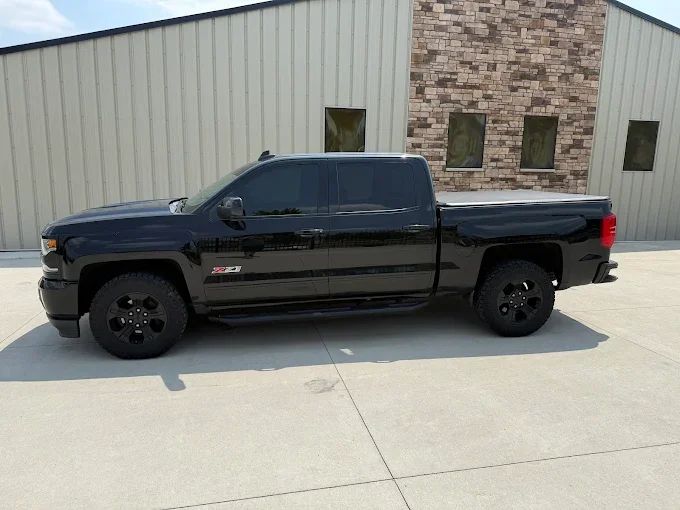 A black pickup truck parked in front of a beige building with a brick accent wall.