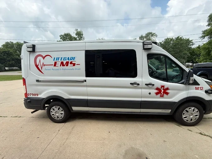 Lifecare EMS ambulance vehicle parked outdoors on a concrete surface, with trees and a cloudy sky in the background.