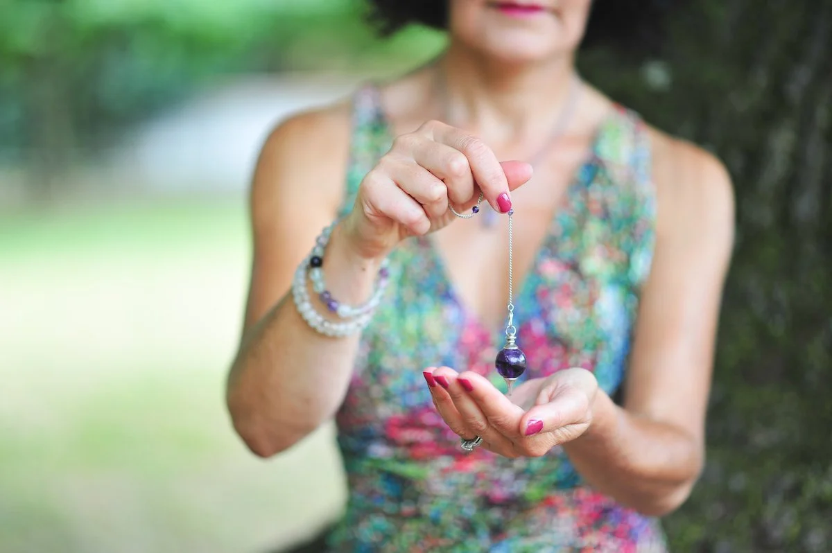 Femme tenant un collier avec une perle violette et des bracelets colorés, affichée en plein air.