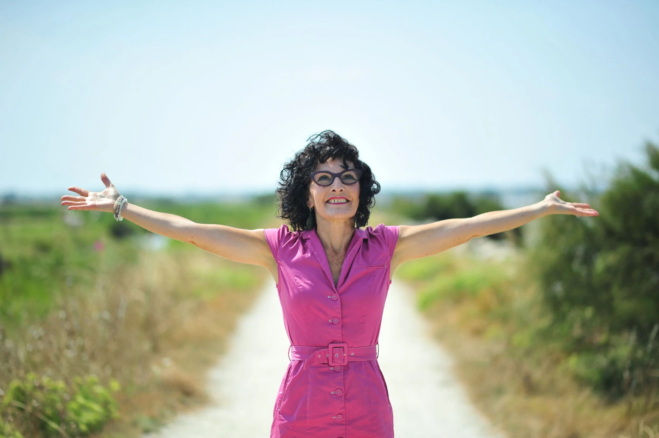 Femme souriante en robe rose avec bras ouverts dans un champ ensoleillé