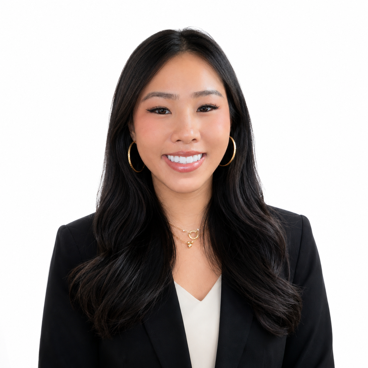 A young Asian woman with long black hair smiling, wearing a black blazer and a white top, standing against a dark grey background.